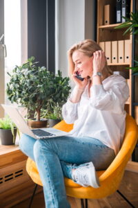 Professional virtual support specialist working on a laptop and phone in an organized home office