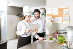 Professional personal chefs evaluating virtual support solutions on tablet in commercial kitchen
