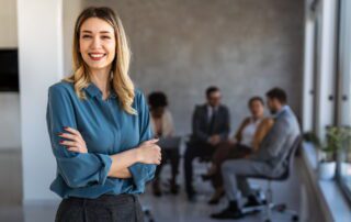 Director standing confidently in an office with meeting in the background