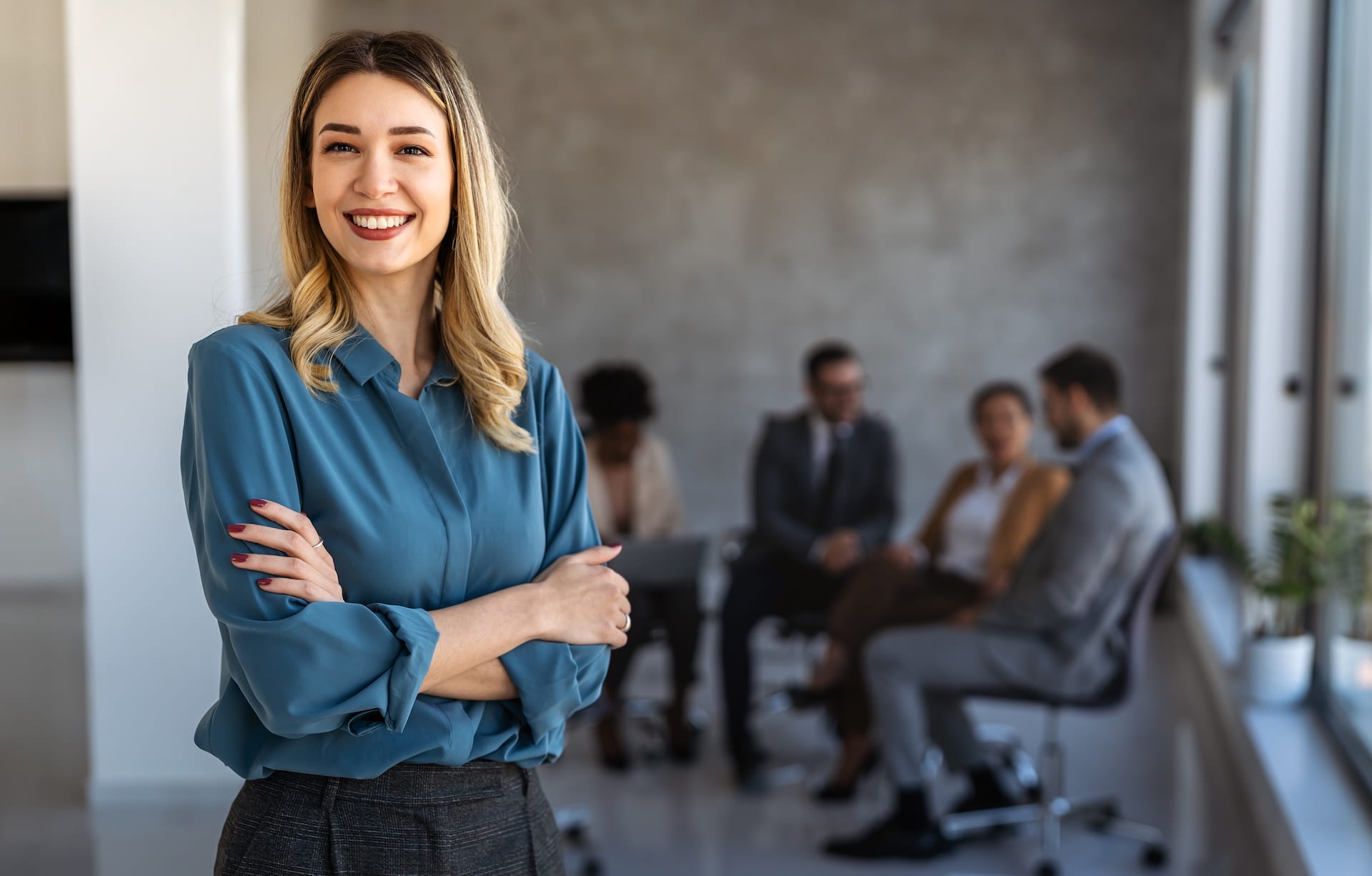Director standing confidently in an office with meeting in the background