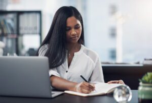 Business leader evaluating where to get a virtual assistant, reviewing information on laptop and taking notes
