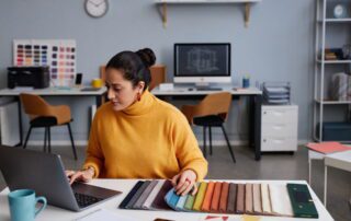 Interior designer at desk with laptop and colorful fabric swatches preparing for virtual assistant support