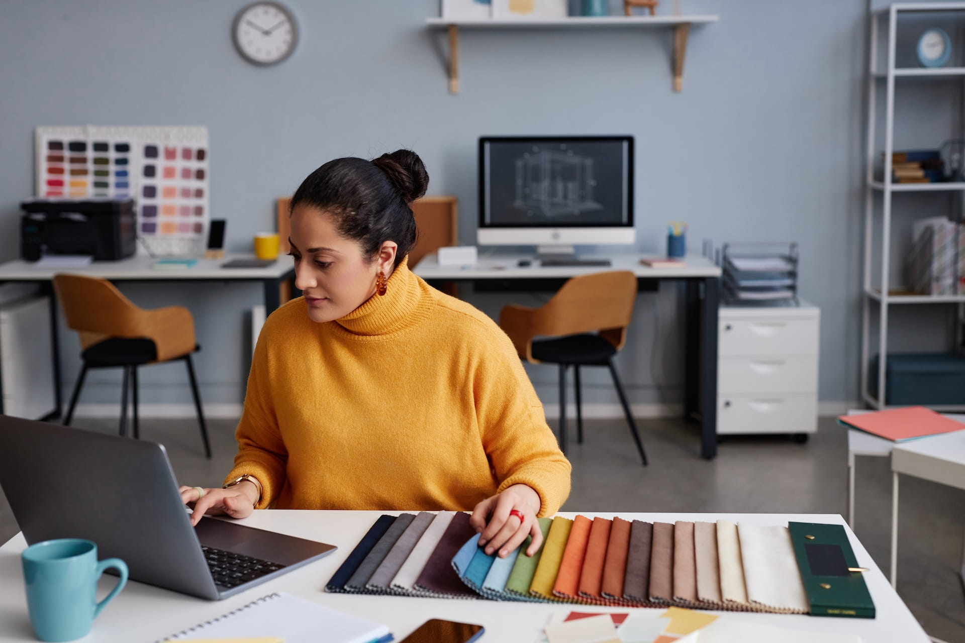 Interior designer at desk with laptop and colorful fabric swatches preparing for virtual assistant support