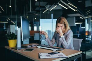 Exhausted business professional experiencing post-layoff workload stress at modern office desk