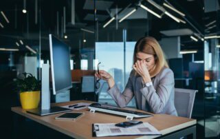 Exhausted business professional experiencing post-layoff workload stress at modern office desk