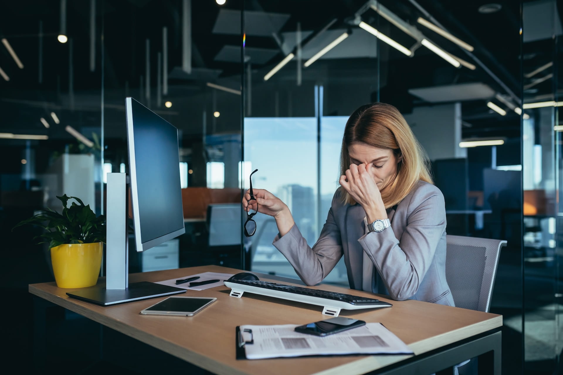 Exhausted business professional experiencing post-layoff workload stress at modern office desk